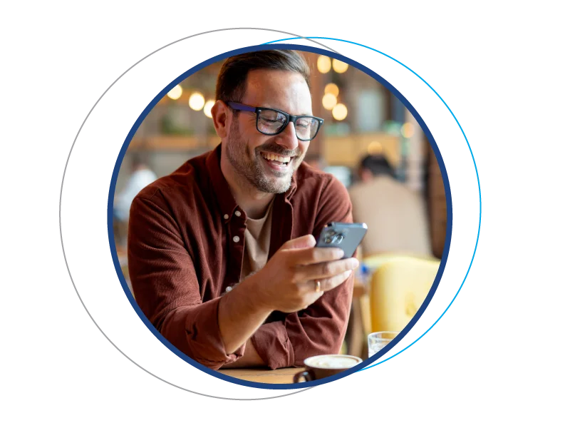 Smiling man checking his smartphone at a café, representing flexible savings options with a Service Credit Union Share Certificate.