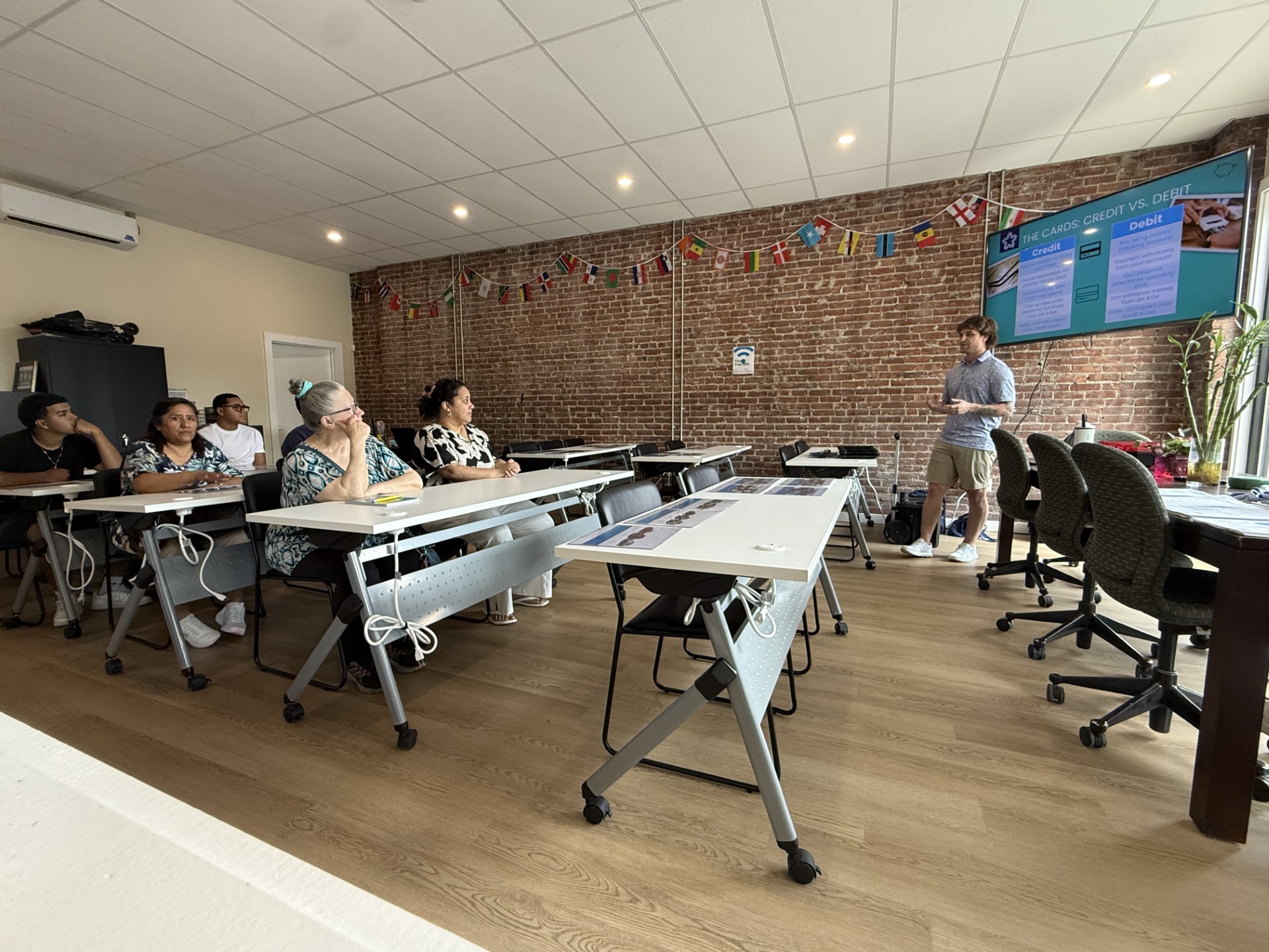 Instructor leads a financial education workshop on credit and debit cards for attendees seated in a classroom.