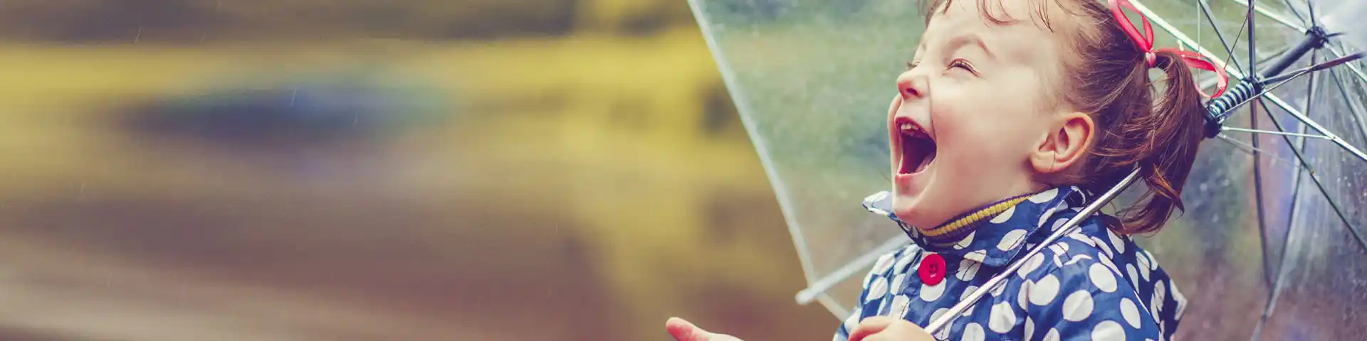small child laughing while its raining, holding an umbrella